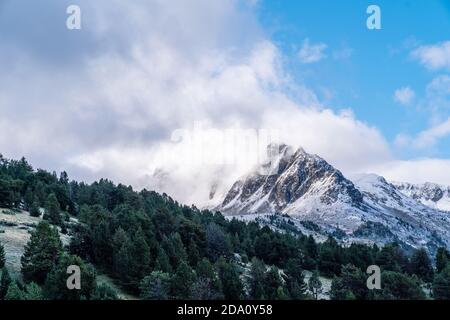 Picturesque panoramic landscape of green valley with coniferous forest against majestic snow covered peaks of Pyrenees mountains under blue cloudy sky Stock Photo
