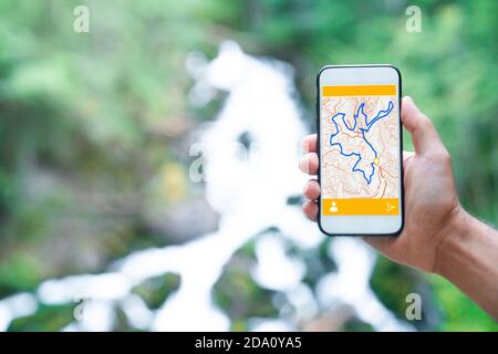 Cropped unrecognizable man traveler using smartphone browsing on map app standing on slope of amazing landscape of green forest with fast river Stock Photo