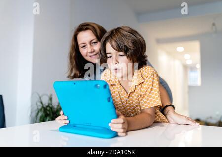 Cheerful kid with bright netbook at table near content mother in house with glowing lights Stock Photo