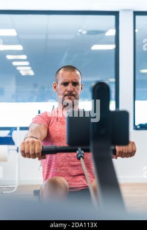 Concentrated athletic male doing exercises on rowing machine while training in modern gym Stock Photo