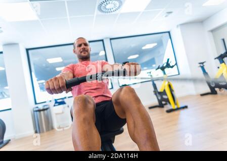 Concentrated athletic male doing exercises on rowing machine while training in modern gym Stock Photo