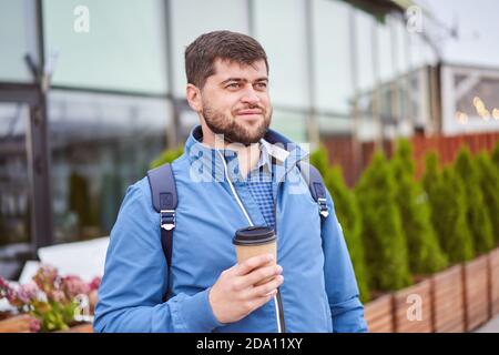 Bearded man drinks coffee from paper cup outdoors. Stock Photo