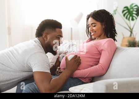 Black father holding headset on pregnant woman belly Stock Photo
