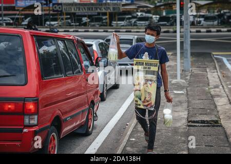 Kuala Lumpur, Malaysia. 08th Nov, 2020. A young man wearing a face mask with a sign hanging around his neck reading 'Mango Pickle Sour Plum' approaches vehicles amid traffic to make some sales with the vehicle owners.The government of Malaysia has implemented an extension of the Conditional Movement Control Order (CMCO) from November 9 to December 6 2020, in most states as Covid-19 cases raise in the nation. Credit: SOPA Images Limited/Alamy Live News Stock Photo