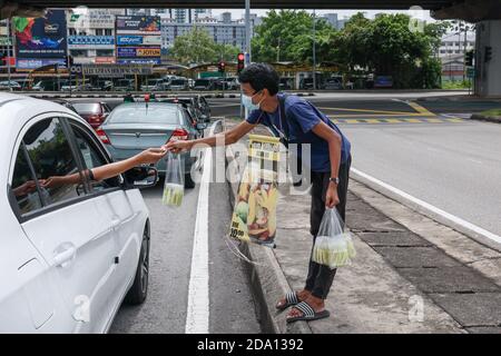 Kuala Lumpur, Malaysia. 08th Nov, 2020. A young man wearing a face mask with a sign hanging around his neck is seen receiving payment after selling fruits on the road.The government of Malaysia has implemented an extension of the Conditional Movement Control Order (CMCO) from November 9 to December 6 2020, in most states as Covid-19 cases raise in the nation. Credit: SOPA Images Limited/Alamy Live News Stock Photo