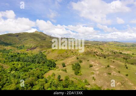 Hills with green grass and blue sky with white puffy clouds. Beautiful landscape on the island of Luzon, aerial view. Stock Photo