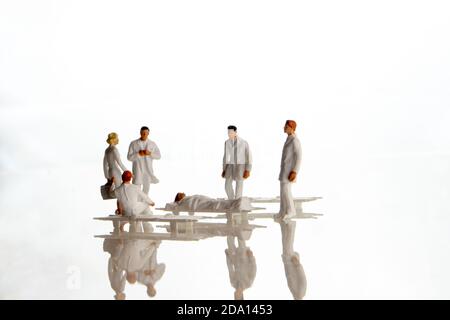 closeup of the team of miniature figurines of special doctor forces and normal doctors having a meeting around a sick person on a strecher with danger Stock Photo