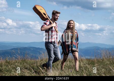 Couple travelers Man and Woman follow holding hands at sunny mountains landscape on background. Couple in love. Stock Photo