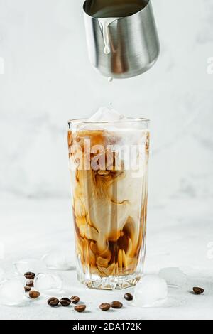 Pouring milk into the glass of iced coffee. Stock Photo