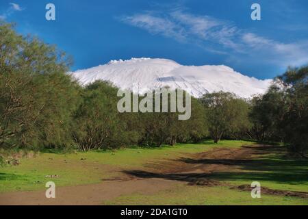 dirt road to Etna Mount snow covered below white low clouds from 'Piano delle Ginestre' typical vegetation of Etna Park in Sicily Stock Photo