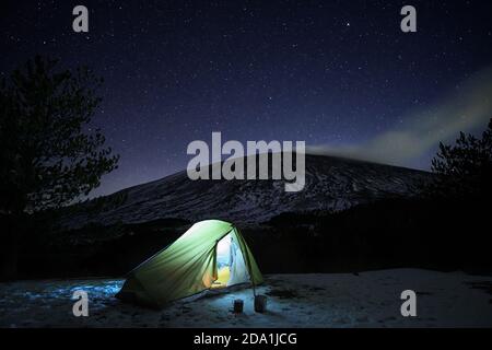 starry sky on green illuminated tent in winter landscape of Etna Park, Sicily Stock Photo