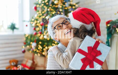 https://l450v.alamy.com/450v/2da1xht/merry-christmas-and-happy-holidays!-cheerful-grandma-and-her-cute-grand-daughter-girl-exchanging-gifts-granny-and-little-child-having-fun-near-tree-i-2da1xht.jpg