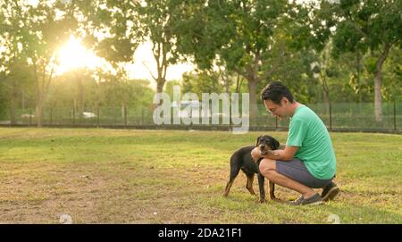 Man playing with pet dog in the park, sunset nature background. Stock Photo
