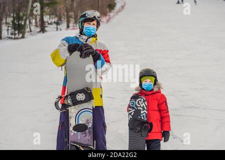 Snowboard instructor teaches a boy to snowboarding wearing a medical mask during COVID-19 coronavirus. Activities for children in winter. Children's Stock Photo