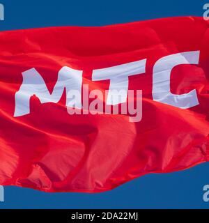 Red flag waving in wind with text in Russian: MTS Mobile TeleSystems, abbreviation mobile operator Russian Federation. Brand flag on background sky Stock Photo