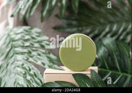 round green cosmetic jar on podium and green tropical leaves around, natural cosmetic layout, selective focus Stock Photo