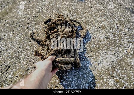 Hand extend to an old and frayed rope standing in a mess. Old rope standing on the concrete floor and its shadow is shown. Stock Photo