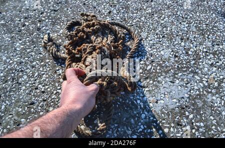 Hand extend to an old and frayed rope standing in a mess. Old rope standing on the concrete floor and its shadow is shown. Stock Photo