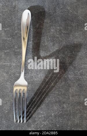 fork lying on textured gray background with an unusual shadow, close up, flat lay, top view Stock Photo