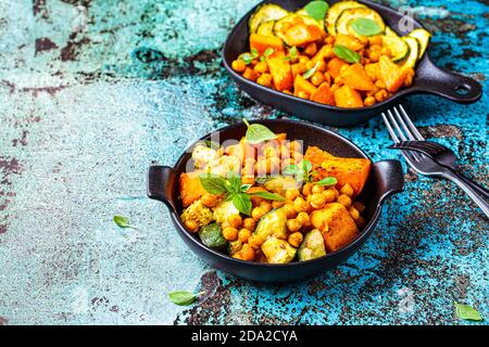 Baked sweet potato, zucchini and chickpeas in cast iron pans, blue background. Baked vegetables. Healthy food concept. Stock Photo