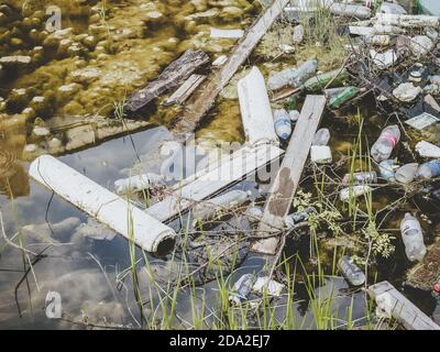 Dirty waterlogged water with silt and grass is littered with plastic bottles with pieces of wood and other waste Stock Photo