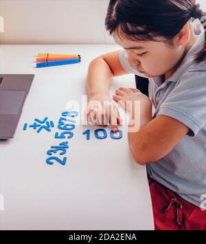 Asian schoolgirl studying homework math during her online lesson at home with laptop at home. New normal.Covid-19 coronavirus. Social distancing. Stock Photo