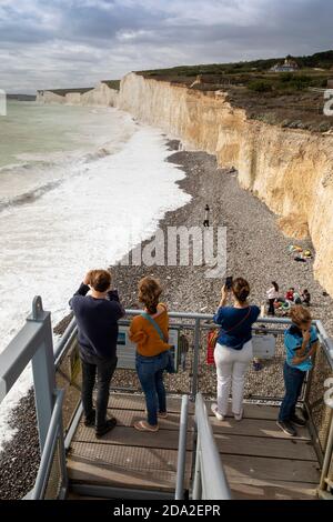 UK, England, East Sussex, Birling Gap, visitors on steps to beach enjoying view west along chalk cliffs towards Seven Sisters and Cuckmere Haven Stock Photo