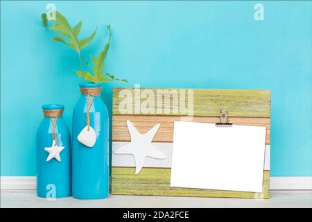 Blank greeting card on rustic wooden clipboard mockup, template with fern leaves in vase and maritime decoration  in front of blue wall, White area is Stock Photo