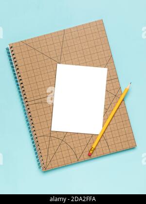 White card on squared notebook with pencil mockup. Blank area masked with clipping path, Turquoise background, high angle view. Stock Photo