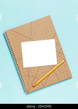 White card on squared notebook with pencil mockup. Blank area masked with clipping path, Turquoise background, high angle view. Stock Photo