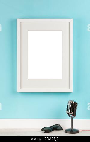 Vertical picture frame with matte on turquoise wall  mockup background template with classic studio microphone and sunglasses, rock music concept Stock Photo