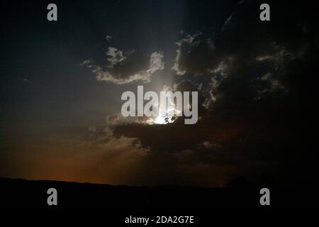 sun shines behind a dark wall of clouds in the sky Stock Photo