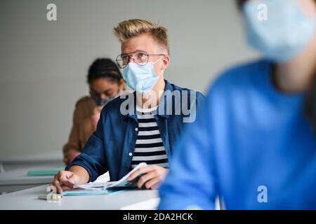 Portrait of young students with face masks at desks at college or university, coronavirus concept. Stock Photo