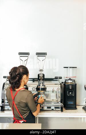 Back view of a female barista making coffee. Woman in apron working in a small coffee shop. Stock Photo