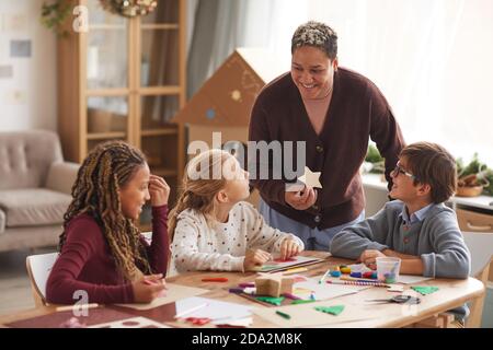 Portrait of smiling African-American woman teaching art class with multi ethnic group of children making handmade Christmas cards in school