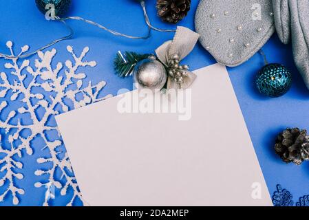Christmas composition with white snowflake, Christmas tree toy, pine cone and white blank paper sheet for text. Christmas blue background with copy Stock Photo