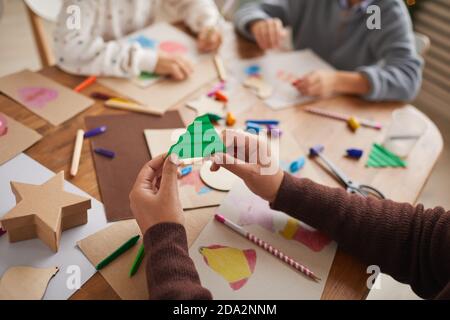 Close up of unrecognizable girl holding paper Christmas tree while doing art and craft project with group of children, copy space Stock Photo