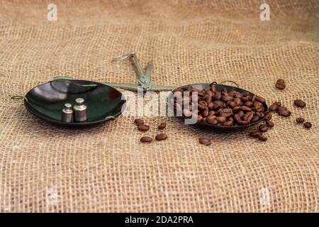 Roasted coffee beans, weighed on an antique hand scale with weights, lying on a table covered with burlap. Stock Photo