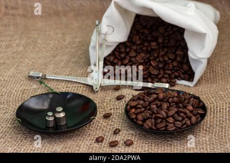 Roasted coffee beans, weighed on an antique hand scale with weights, lying on a table covered with burlap. Stock Photo