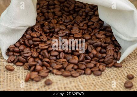 Roasted coffee beans, weighed on an antique hand scale with weights, lying on a table covered with burlap. Stock Photo