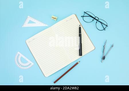 Open notebook, ballpen, pencil, sharpener, rulers, and eyeglasses isolated on a blue surface Stock Photo