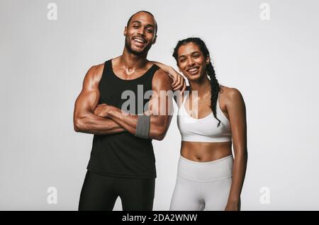 Cheerful male and female athlete standing together at gym. Smiling woman standing with her hand on shoulder of male friend. Stock Photo