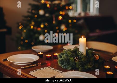 Christmas candles in advent wreath with plates on dinner table. Scandinavian home decorated for Christmas dinner. Stock Photo