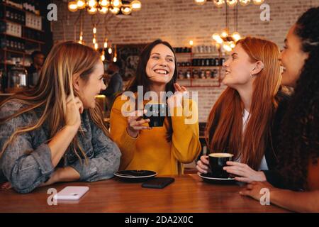 Group of friends sitting and talking at a coffee shop. Young women sharing some funny gossips with friends. Stock Photo