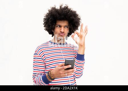 Portrait young man with afro hair listening to music on mobile phone giving ok sign Stock Photo