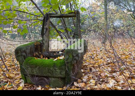 Old, damaged armchair in the autumn surroundings of trees. Destroyed armchair in the autumn forest.Garbage in the forest - ecology. Stock Photo