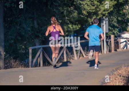 Young man in blue t-shirt and young woman in purple t-shirt jogging at park Stock Photo