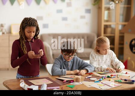 Waist up portrait of teenage African-American girl taking photo of handmade picture to post on social media during art class, copy space Stock Photo