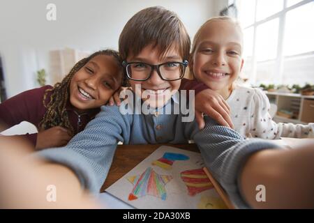 Portrait of three happy children smiling at camera while taking selfie photo in school Stock Photo
