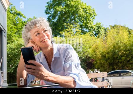Close up portrait happy middle age woman holding mobile phone outside Stock Photo